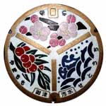 薄いピンク色の町の花の梅、赤い果実の町の木やまもも、瀬戸内海の波と波頭を配した旧御津町のシンボルがデザインされたマンホールの写真