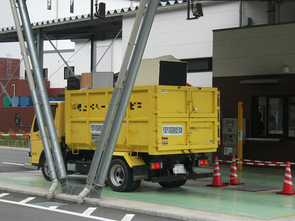 荷台の部分にたくさんの荷物が積まれている黄色いトラックが停車し計量している写真