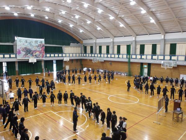 体育館の中でいくつかに分かれた生徒たちで円を描くように立っている様子の写真