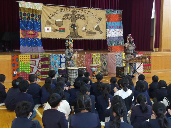 民族衣装を着た2名の方が、座っている児童たちの前に立っている写真