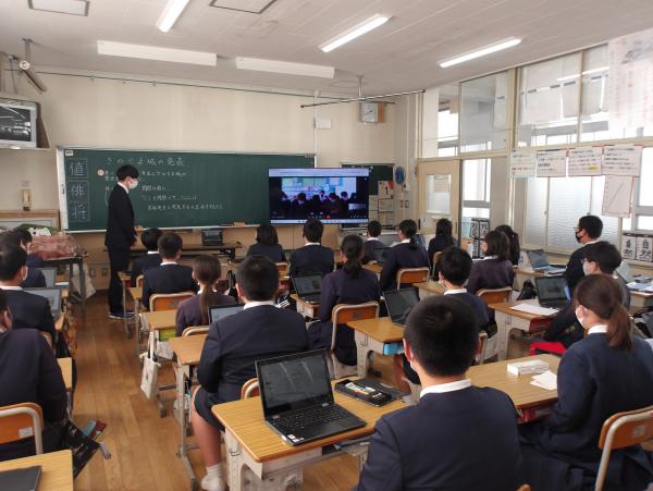 教室で席に座っている児童たちが、他の学校の児童たちが映っている黒板横のモニターを見ているところを後方から撮影した写真