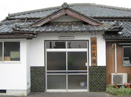 白い外観と灰色の瓦屋根で木製の大きな表札が玄関横にある構公民館の写真