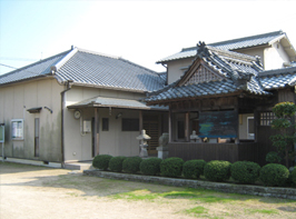 神社のような建物が併設され丸く小さな庭木の植えられている田井農業構造改造センターの写真