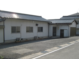 道路わきにある、白い外観と灰色の瓦屋根の長屋の北沢公民館の写真