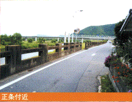 大きな橋がかかる揖保川沿いの細い道路に畳堤が設置された正条付近の写真