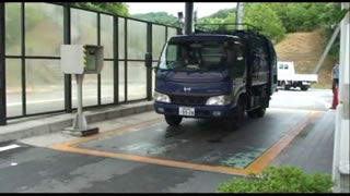 青いゴミ収集車が計量器のオレンジ色の枠内に停車している写真