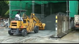 黄色の重機に乗った男性作業員が、置き場にスラグを山積みに置いている様子の写真