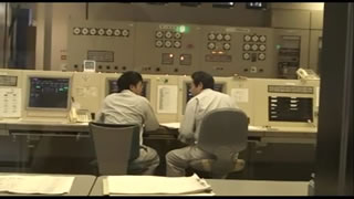 2人の作業員が椅子に座って話し合っている前にコンピューターが設置されている中央制御室内の写真