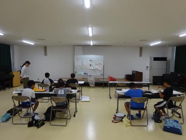 前方にホワイトボードが置かれた室内で、児童達が長机に2名ずつ座り絵を描いている写真