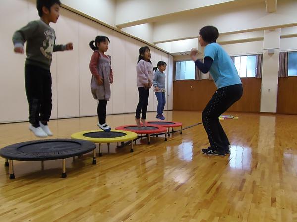 丸い一人乗りのミニトランポリンが4つ横の並べられ4人の幼児がミニトランポリンで跳んでいる前で講師が指導しているキッズスポーツリズムの写真