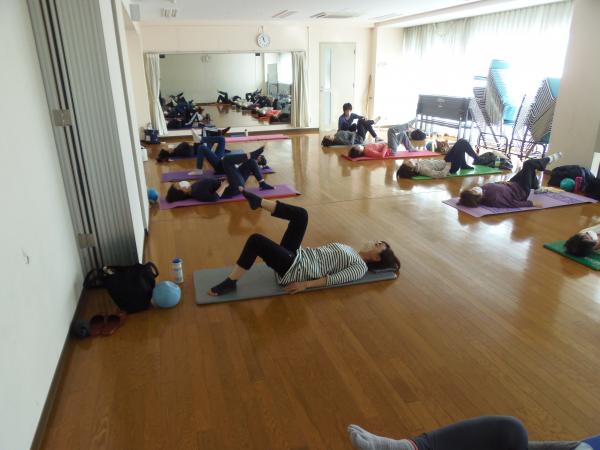 両側に5人づつヨガマットを並べその上で仰向けになり右足を上げている参加者と1人の方に講師がアドバイスをしていピラティスの写真