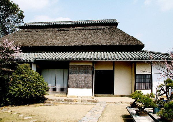 盆栽やピンクの花が咲く龍野藩西組大庄屋の八瀬家住宅の庭から家全体を撮影した写真
