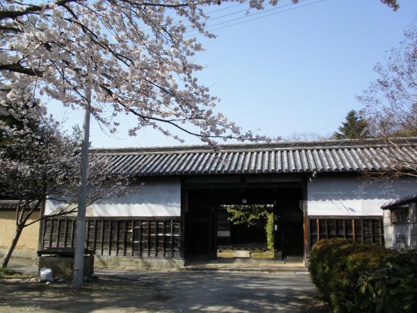 手前に花がっ咲き誇り奥に白と茶色の堀家長屋門の外壁を写した写真