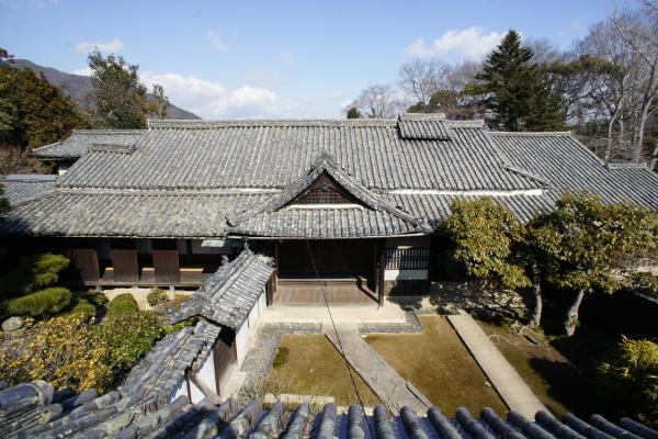 周囲を木々に囲まれた広い敷地内に建つ国指定重要文化財「堀家住宅」の主屋を高所から撮影した写真