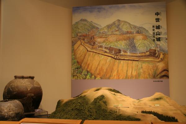 「中世城山城」と書かれた絵画の前に壺と山の模型が置かれている写真