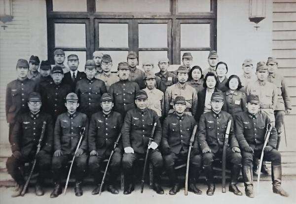 軍服を着た1列目の7名は刀を足元に立てながら座り、2列目3列目4列目の人達は立ちながら記念撮影をしている十研職員の白黒写真