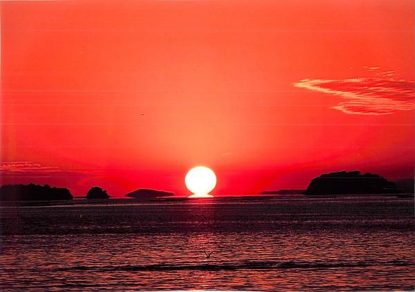 海の上に浮かぶ今にも沈みそうな夕日と赤く染まった空の写真