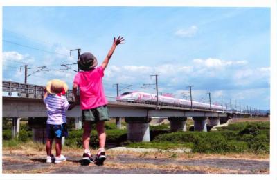 新幹線に向かって手を振る子供たちの後ろ姿を撮影した写真