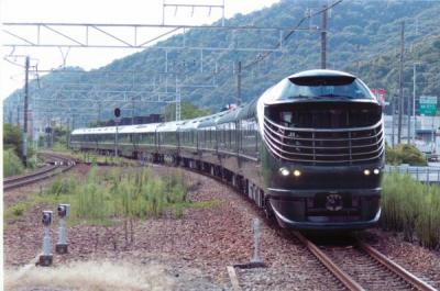 木が生い茂る緑の山の麓の線路を走る黒い電車を正面から撮影した写真