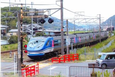 踏切を通り過ぎる青い電車と停まって待つ自動車を撮影した写真