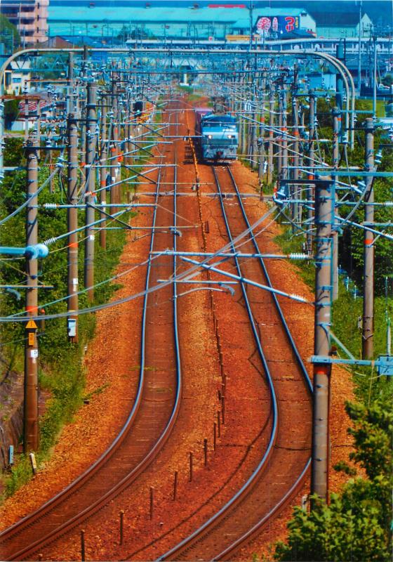 まっすぐ伸びた線路の奥からライトを点けた電車が迫ってくる写真