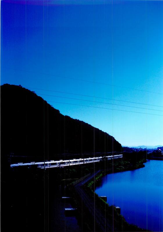 藍色に染まる空と川の間を走る銀色に輝く電車を撮影した写真