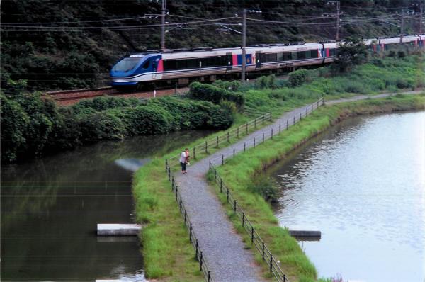 中央に歩道が掛かる川の奥を颯爽と走り向ける青い電車を撮影した写真