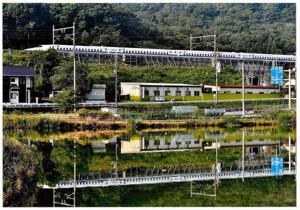 水が張った田んぼに鏡のように映る建物や白い新幹線を撮影した写真