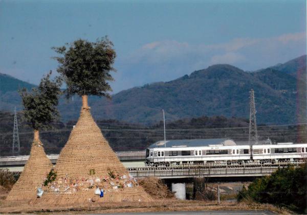 正月に焼いてしまうトンドの奥に掛かる橋の上を走る白い電車を撮影した写真