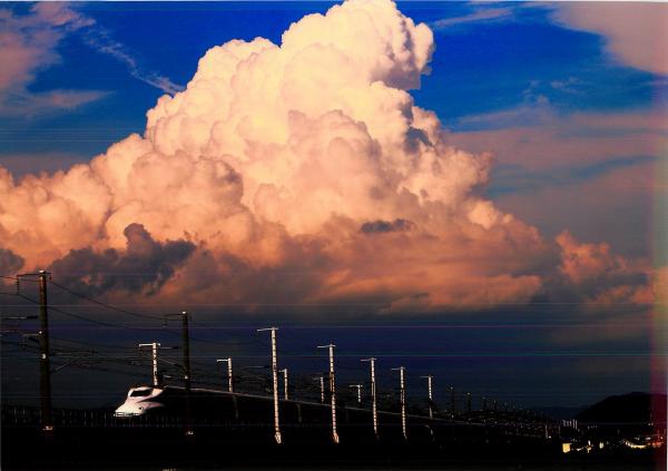 夏の線路を風のように早く走る白い新幹線の上に広がっている大きな入道雲を撮影した写真