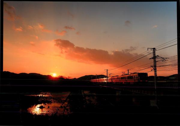 夕日が山に隠れ光がなくなっていく線路を静かに走る電車を撮影した写真