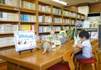 横にずらりと並んだ本棚と、そのそばにある長机の席に座る小さな子どもを写した写真