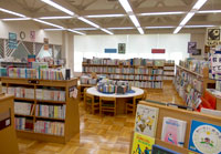 たくさんの本棚や、椅子付きの大きな丸型の机などが置かれた新宮図書館内の館内を写した写真