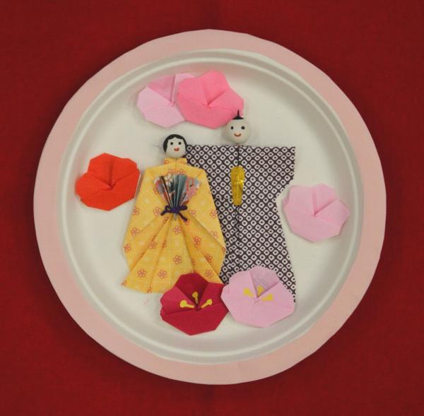 紙皿の上にピンク色の梅の花と、お内裏様とお雛様が色紙で作られた作品の写真