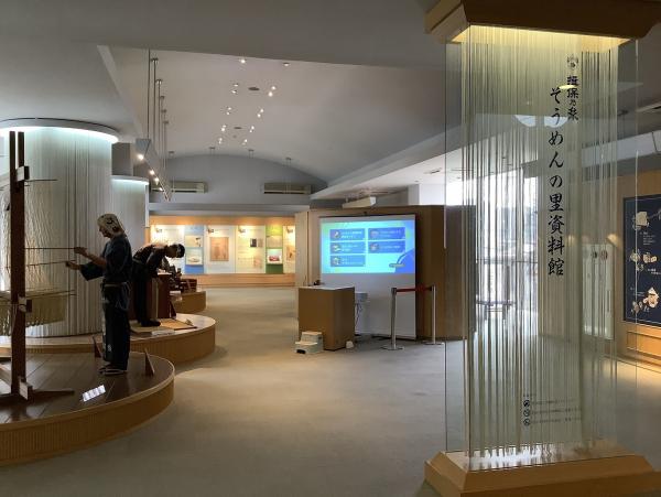 そうめんをつるして長い箸で広げている様子の模型や資料が展示されているそうめんの里資料館内部の写真