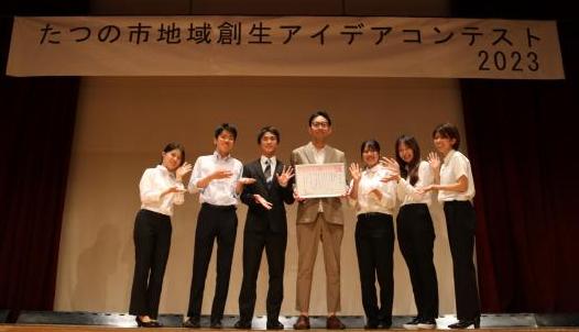 優秀賞を受賞した兵庫県立大学橋本ゼミAチームの皆さんが、舞台の上に立ち賞状を持って横一列に並んでいる写真