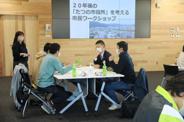 4名の参加者が同じテーブルの席に座って真剣に話し合いをしている様子を写した写真
