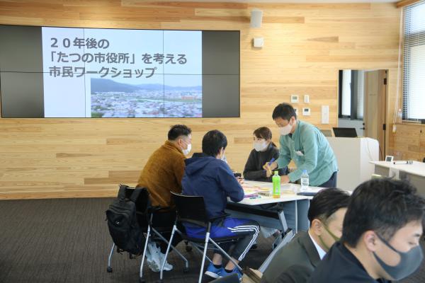 4名の参加者が同じテーブルの席に座って模造紙に付箋を貼りながら話し合いをしている様子を写した写真
