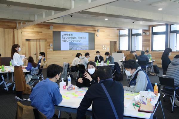参加者たちが広い部屋で複数のグループに分かれ、行政サービスのあり方について話し合いをしている様子を写した写真