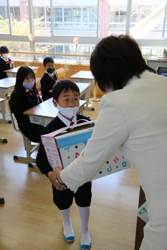 スーツ姿の男の子が女性から箱に入った学用品を受け取ている写真