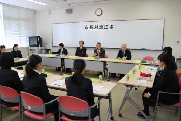 スーツを着た参加者達が設置された席に座り、室内前方のホワイトボードの前の席に市長や関係者が座り市長対話広場が行われている様子写真