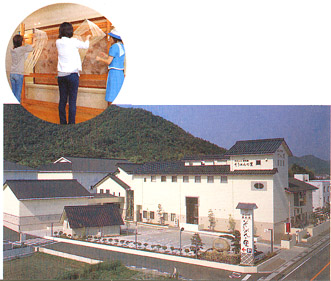 入り口に大文字で「そうめんの里」と書かれた看板が設置され、広い敷地内に建つ白壁の揖保乃糸 資料館の建物と、2名の女性がそうめんを伸ばす体験を行っている写真