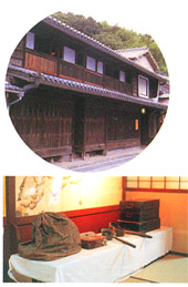 大きな古い町家の本瓦葺きで二階建ての建物外観と、白いクロスが掛けられた長机の上に黒色の箱などの昔使用していた道具が並んでいる写真