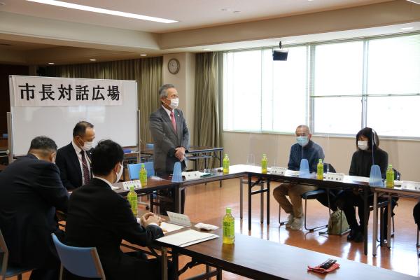 参加者が席に座り、ホワイトボードの前に立っている男性が話をしている様子の写真