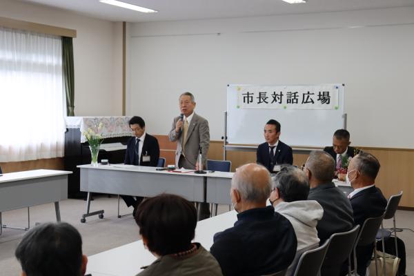 「市長対話広場」と書かれた紙がホワイトボードに貼られ、正面に立っている男性がマイクを持ち話をしている写真