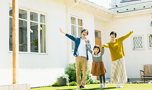 夫婦と女の子の写真。夫婦の中心に女の子がおり両親と手をつないでいる。3人の背景には白い家が建っており、庭のような場所にいる。