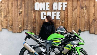 黄緑色のバイクの後ろに横を向いて立っている女性の写真