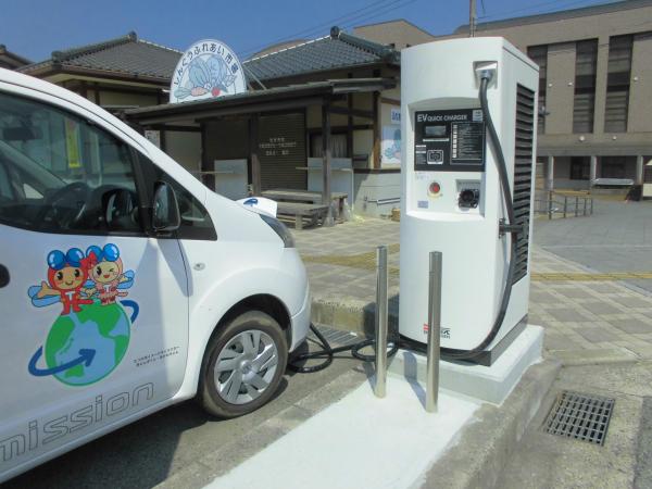 駐車場に設置されている白色の電気自動車用急速充電器と充電している白い車の写真