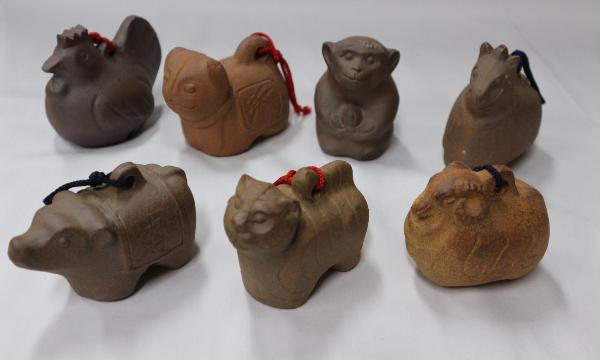 白色の壁際に7つ置かれた、土鈴と言うこげ茶色の置物の写真