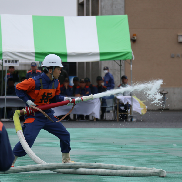 たつの市の消防団員の男性が、大会の競技で、消防用ホースを両手で持って前方に放水している写真